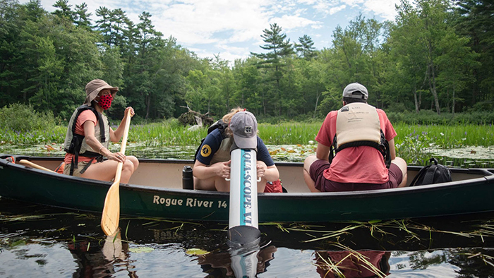 Three people in a canoe while person in the middle looks into the lake