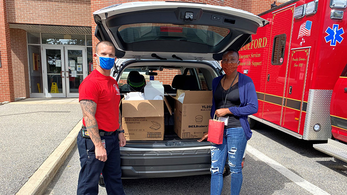 Two volunteers stand by an open car trunk full of donations