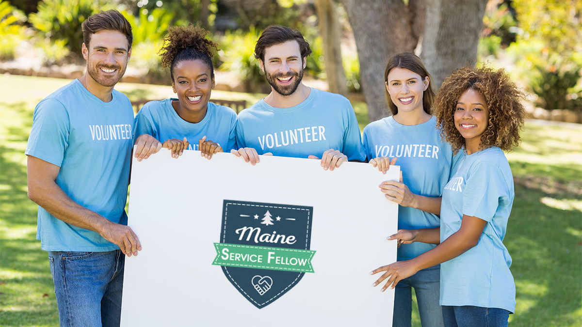 A group of volunteers in a park on a sunny day posing for a photo while holding a large sign