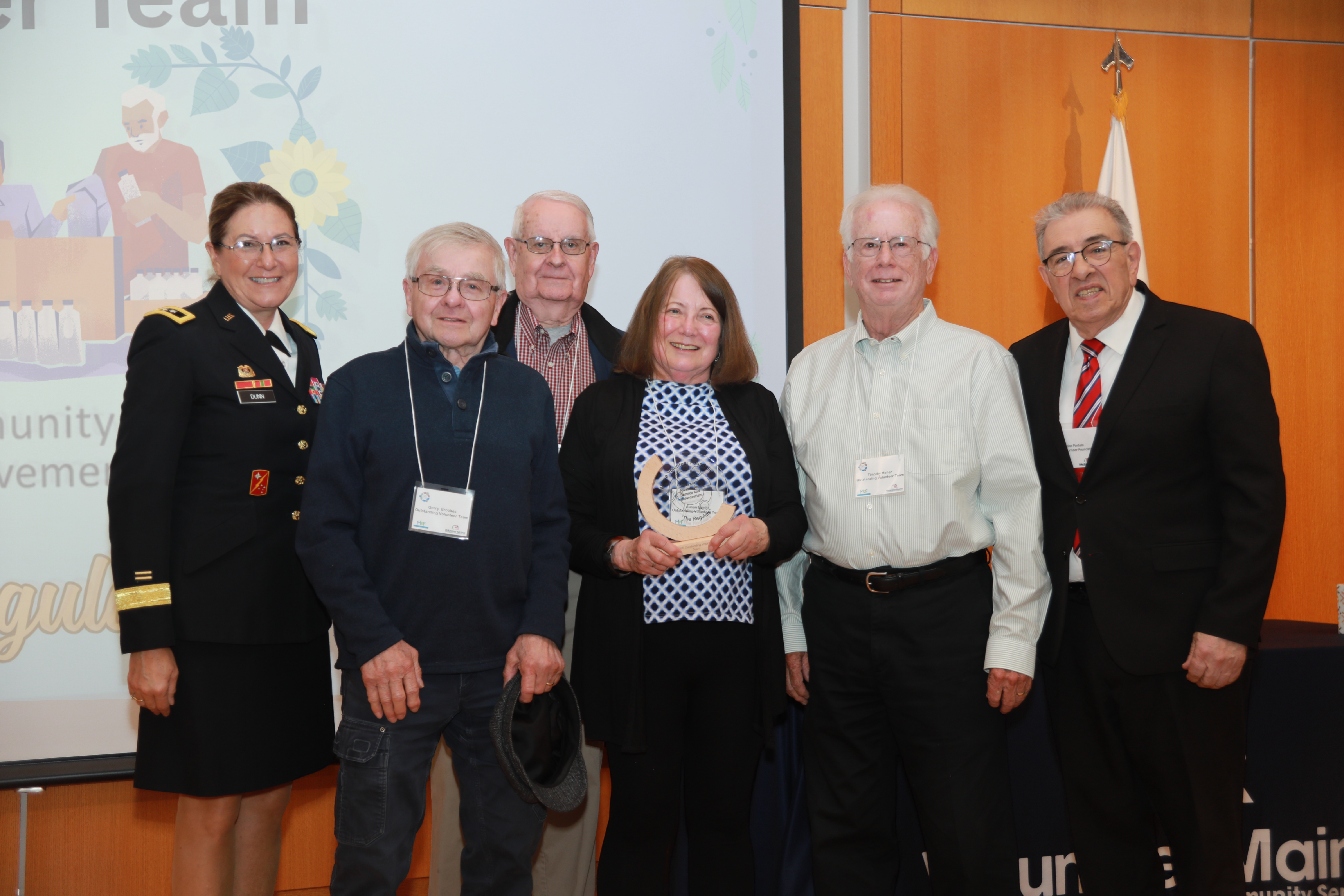 Major General Diane Dunn stands next two two elderly men, one woman, and another elderly man that are part of "The Regulars" who are then next to Maine Volunteer Foundation President John Portela