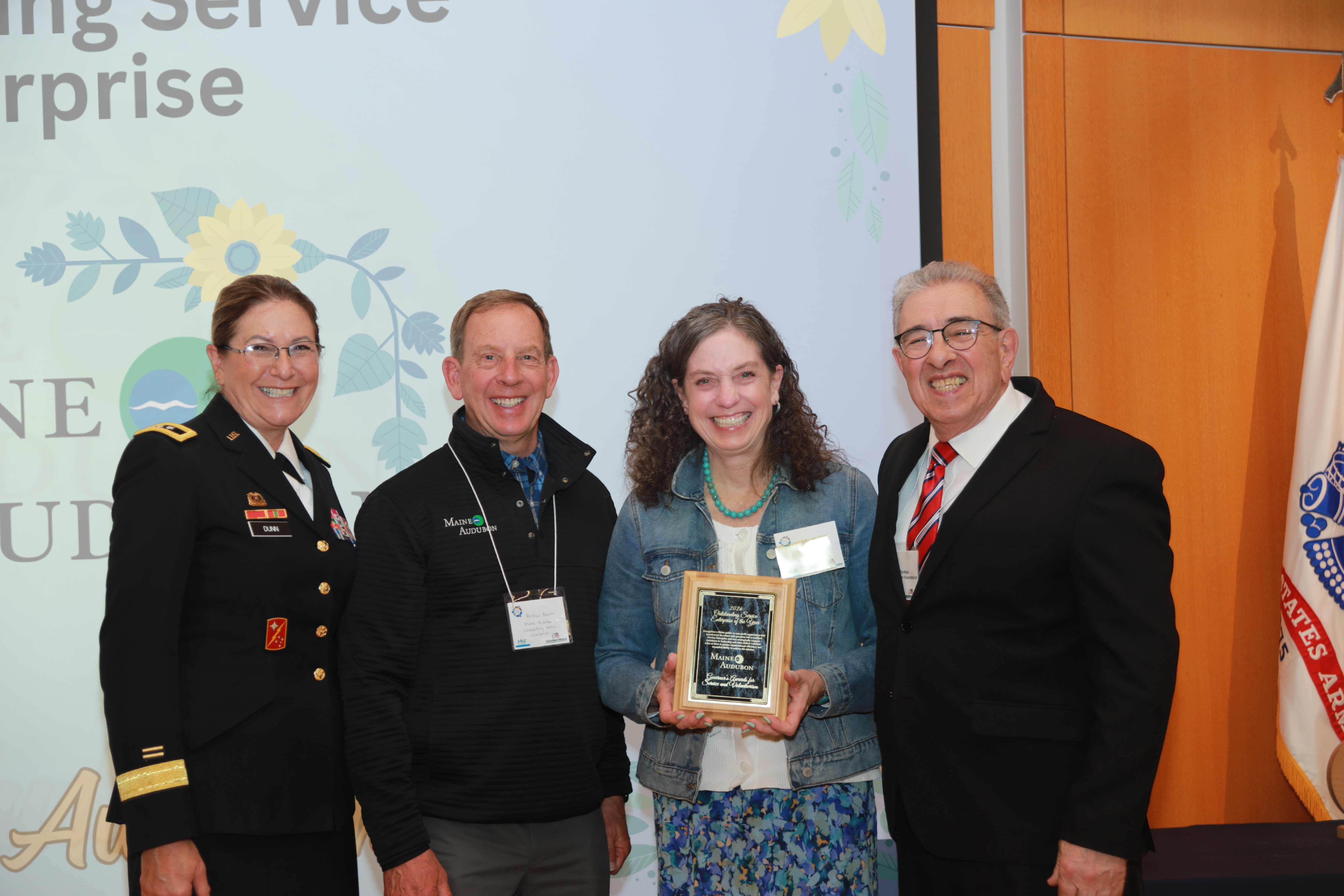 Executive Director Judy Camuso and former Executive Director Andrew Beahm hold a crescent wood and glass award standing in between Major General Diane Dunn and Maine Volunteer Foundation President John Portela