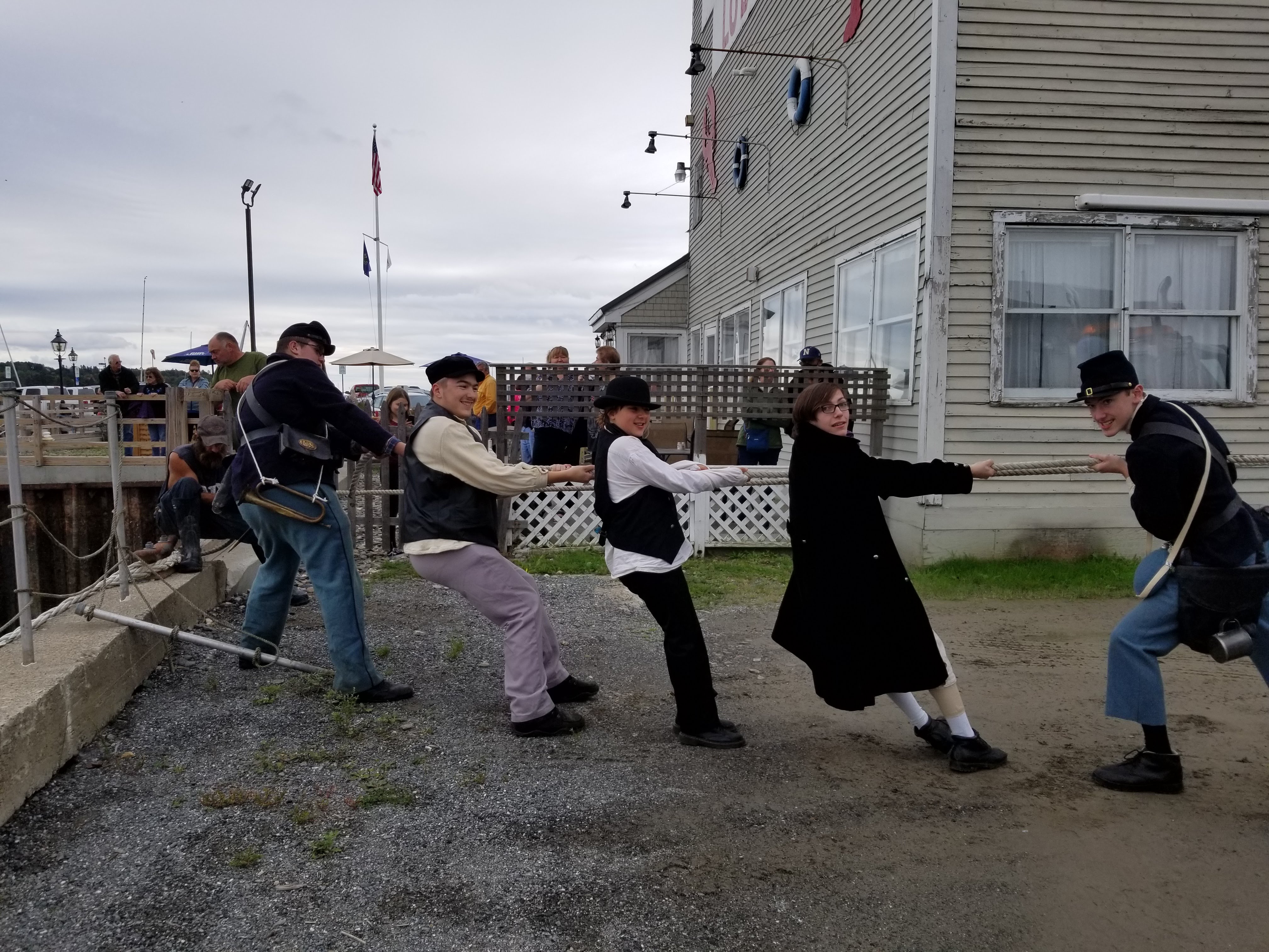 Photo of four individuals pulling a rope at a boatyard while wearing civil-war era costumes