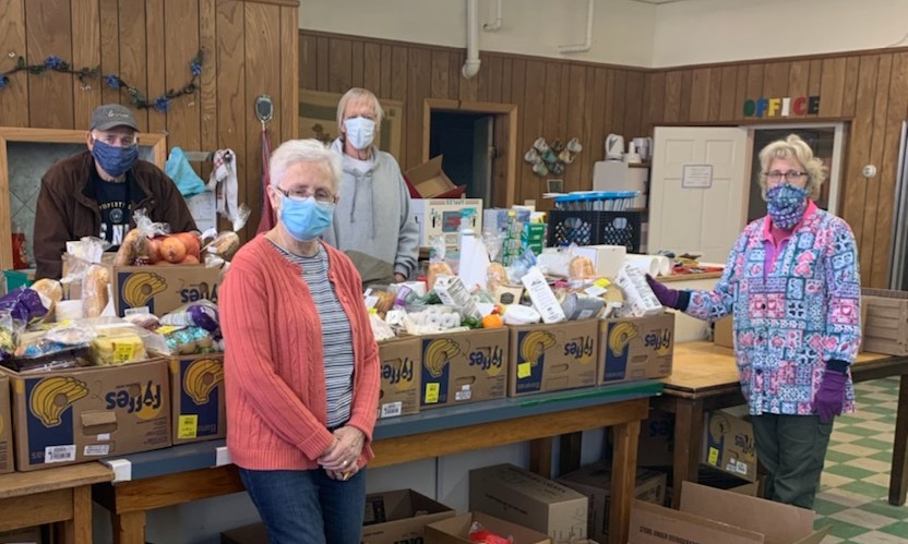 Photo of four individuals spread out around a table full of donations inside a community room