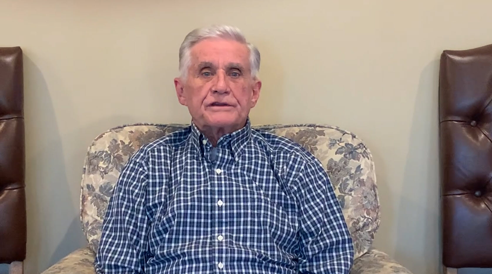 Photo of an individual sitting in a living room delivering remarks for a video