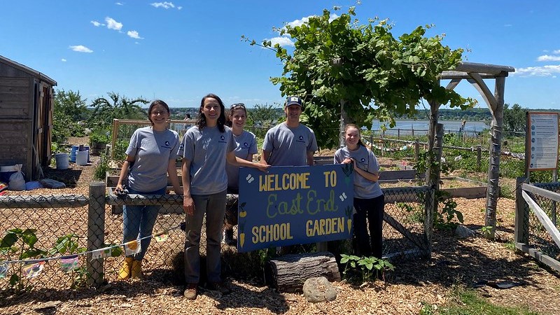 Photo of a group of people posing for a photo by a community garden on a sunny day
