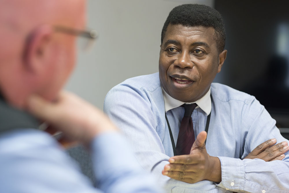 Photo of Luc Nya engaged in a conversation at a table with an individual off screen