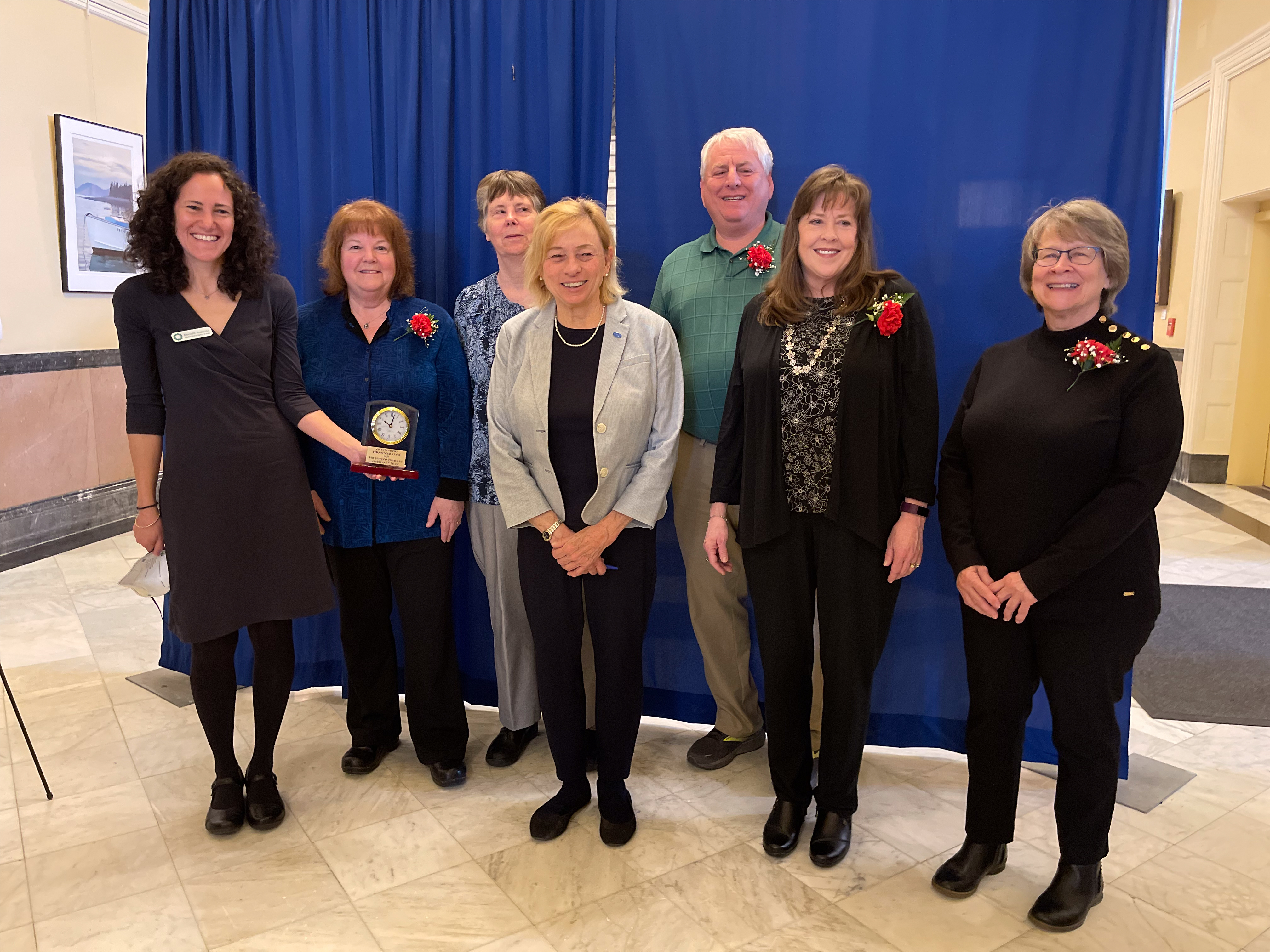 Portrait of members of the Stimulus Check Assistance Team posing in the Maine Hall of Flags with Governor Janet Mills