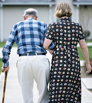 older man with cane holding onto female adult to steady himself as he walks