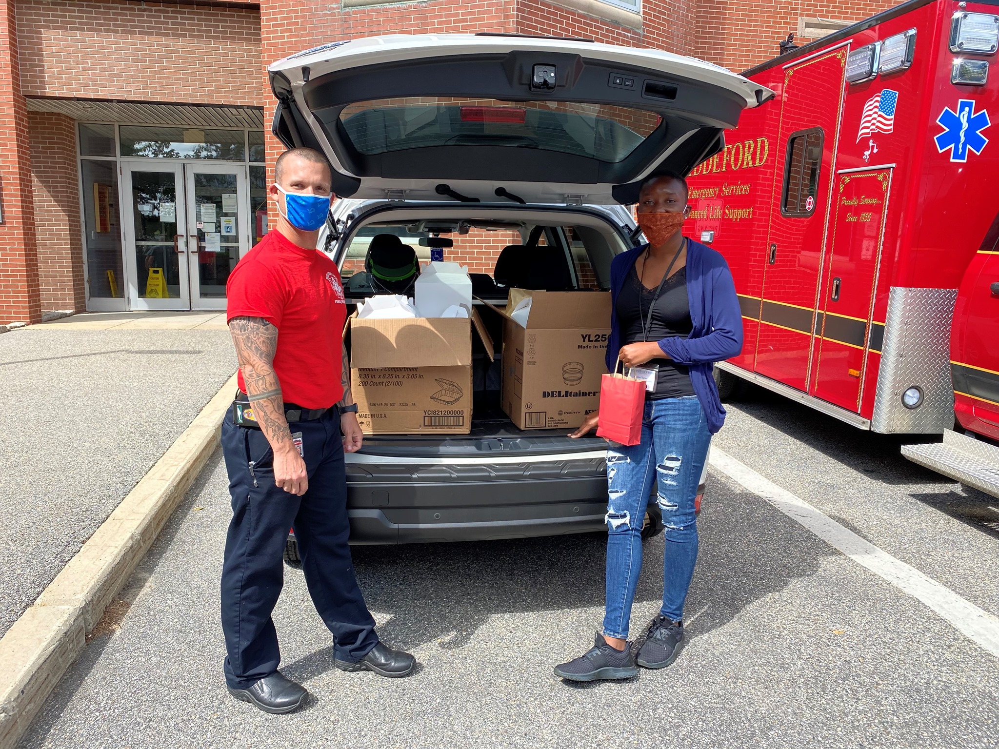Photo of two individuals standing to each side of an open trunk full of donations