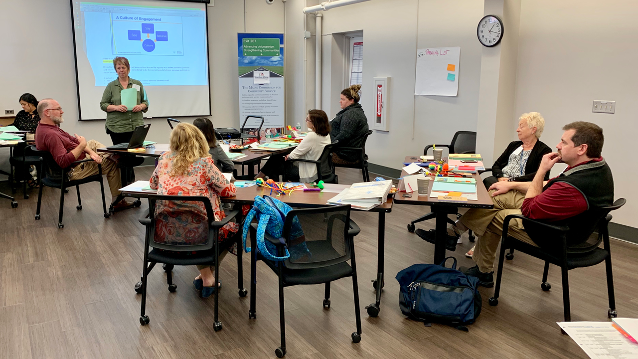 One individual stands at the front of a room to deliver a training course to an audience