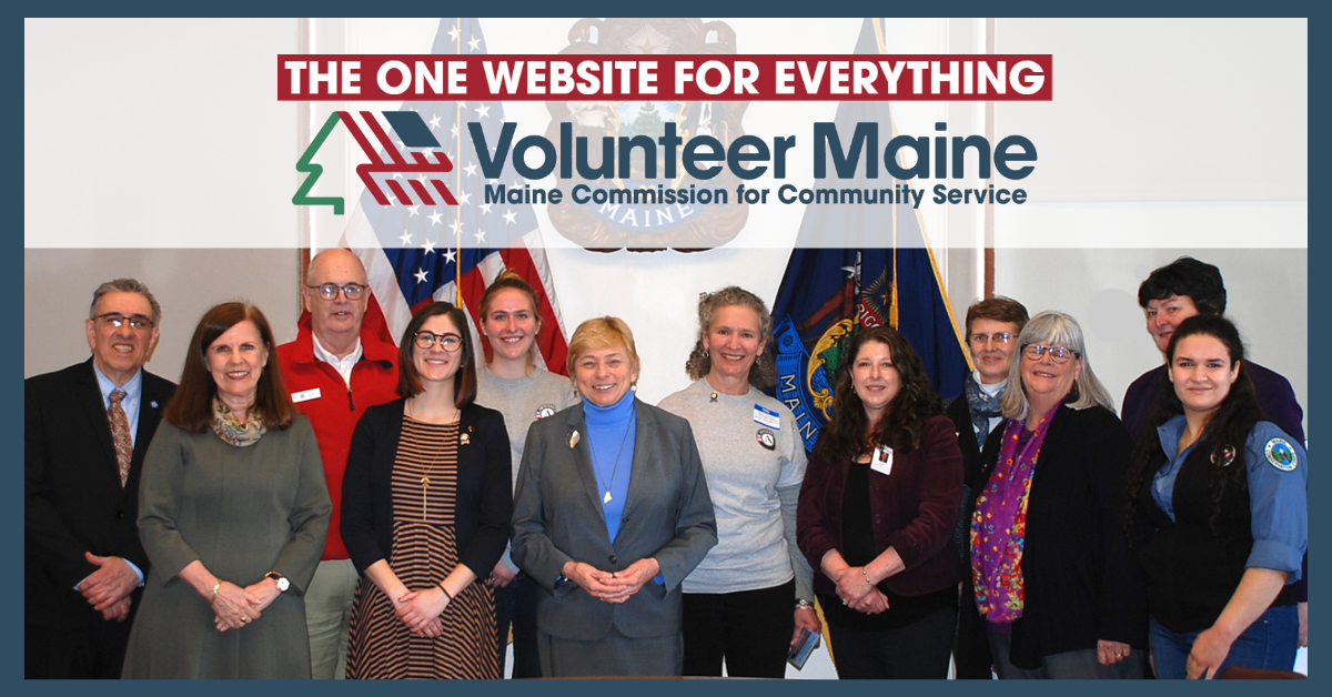 "Group of individuals pose for a group photo in front of a United States flag and the Maine State flag